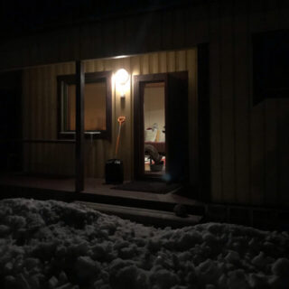 No longer locked out!! Cottage at night with the front door open and lights on inside. Snow is deeper than the porch.